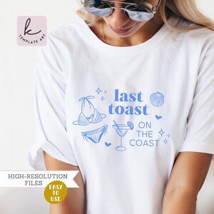 Könnte beinhalten: Weißes T-Shirt mit blauem Text, der "last toast on the coast" lautet. Der Text ist von blauen Illustrationen eines Bikinis, eines Cocktails und einer Muschel umgeben.