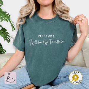 K&ouml;nnte beinhalten: Dunkelgr&uuml;nes T-Shirt mit dem wei&szlig;en Schriftzug "PLOT TWIST: I fell hard for the villain". Das Shirt ist einfarbig und hat kurze &Auml;rmel. Ein Geschenkideen-Aufkleber ist unten rechts sichtbar.