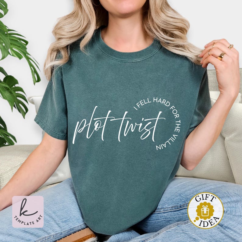 Op de afbeelding: Een tealkleurig t-shirt met de tekst "plot twist" in een cursief lettertype. De zin "I fell hard for the villain" is in een cirkel rond de hoofdtekst geschreven. Het shirt is effen van kleur en heeft korte mouwen.