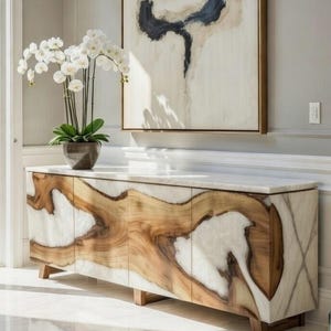 May include: A long sideboard featuring a combination of natural wood grain and white marble panels, supported by wooden legs. On top sits a potted white orchid plant. Above the sideboard hangs a large rectangular painting with abstract black and beige shapes.