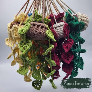 Peut inclure: Une collection de plantes suspendues crochetées dans diverses couleurs, dont jaune, vert clair, vert foncé, bordeaux et crème. Chaque plante est dans un petit pot crocheté avec des feuilles tombantes. Le texte "Plantes Tombantes" est visible.