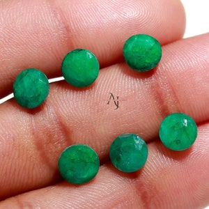 Op de afbeelding: Zes ronde, gefacetteerde, groene edelstenen op een hand. De edelstenen zijn ongeveer 5 mm in diameter.
