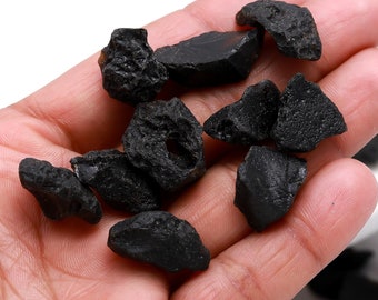 May include: A hand holding a collection of small, black, irregularly shaped stones. The stones have a rough, textured surface.