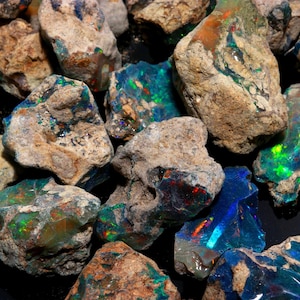 An arrangement of raw Ethiopian opal stones with natural matrix and bright multicolored fire against a dark backdrop.