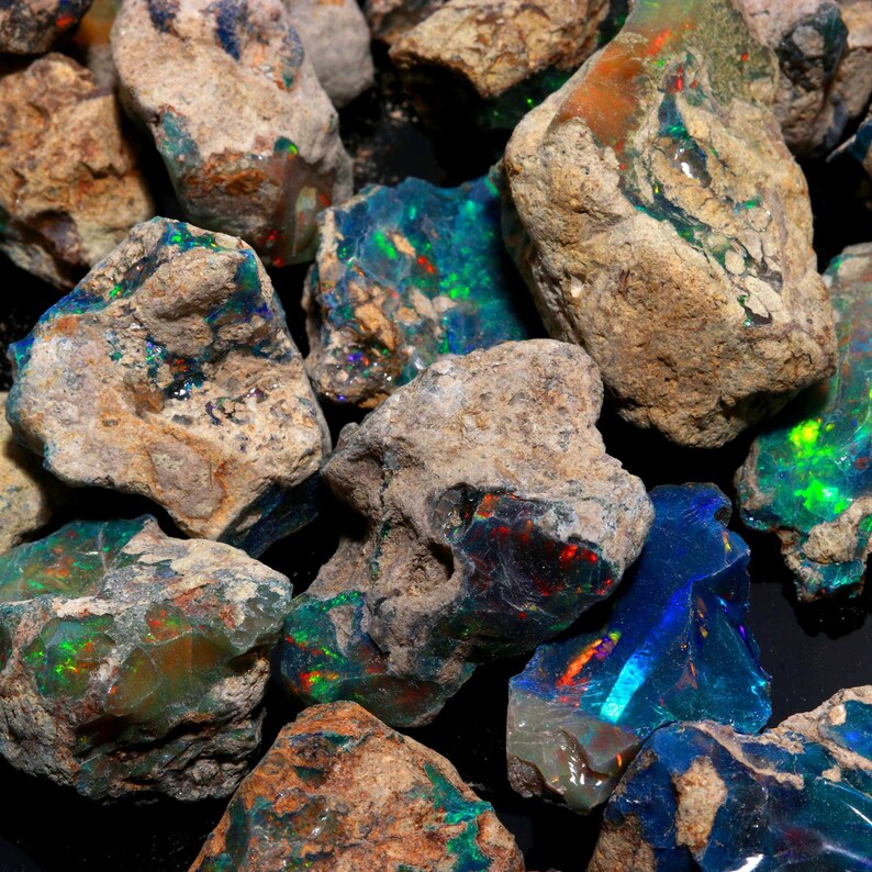 An arrangement of raw Ethiopian opal stones with natural matrix and bright multicolored fire against a dark backdrop.