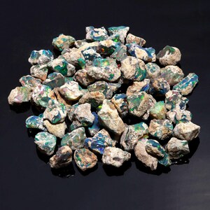 A collection of raw black Ethiopian opal rough stones is scattered on a dark reflective surface.
