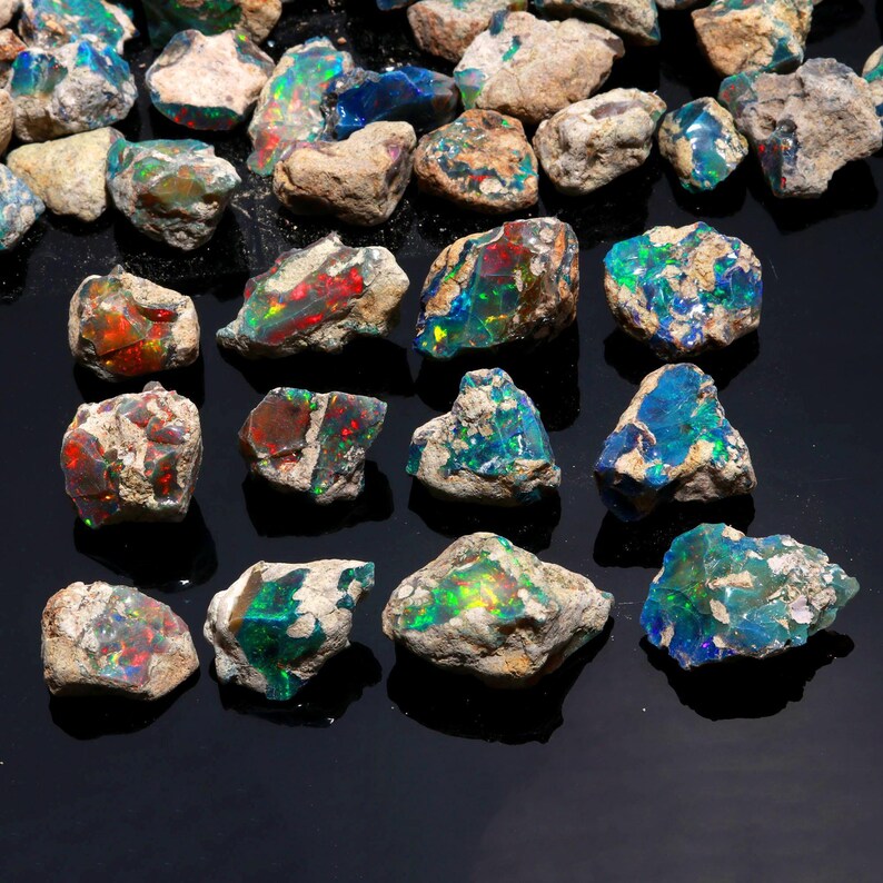A hand holds a large raw black Ethiopian opal stone, showcasing a bright green and blue fire across its surface.