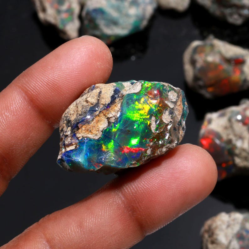 A hand holds a selection of rough Ethiopian opal stones with diverse shapes and colorful fiery inclusions.