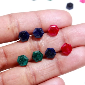 May include: Assortment of faceted gemstone cabochons in various colors, including blue, green, and red. The gemstones are hexagonal in shape and have a polished finish.