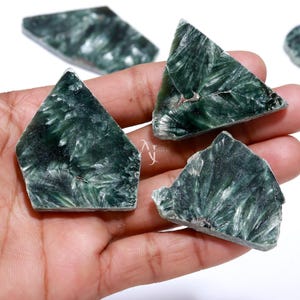 May include: Three polished, flat, triangular-shaped pieces of dark green seraphinite stone. Each piece displays a distinct, feathery, white, and silvery chatoyant pattern radiating from a central point across the deep green, translucent surface.