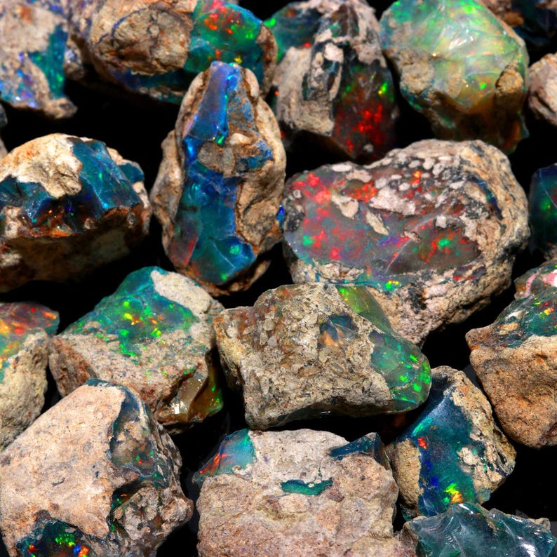 A close-up of rough black opal stones, highlighting raw rock matrix and intense green, blue, and red flashes.