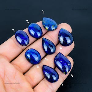 May include: Eight teardrop-shaped lapis lazuli cabochons with gold flecks, numbered 1 through 8. The stones are arranged in a hand, with the numbers visible.