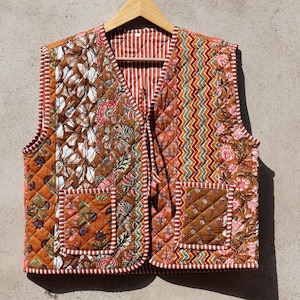 Könnte beinhalten: Eine braune gesteppte Weste mit Bindeverschluss und floralem Patchwork-Design. Die Weste hat zwei Taschen und ist aus Baumwolle.