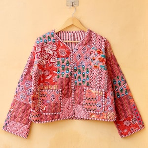 May include: A pink quilted jacket with a patchwork design featuring various floral and geometric patterns. The jacket has a button closure and two pockets.