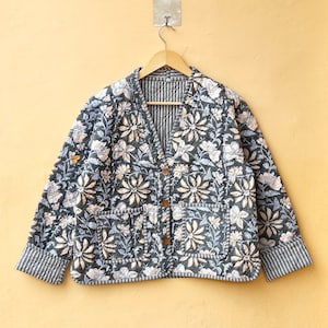 May include: A dark blue quilted jacket with a floral print and a button closure. The jacket has two pockets and a striped lining.