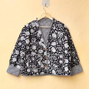 May include: A black and white floral print button-up jacket with a striped lining and two pockets. The jacket is hanging on a hanger against a pale yellow wall.