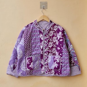 May include: A purple quilted jacket with a floral print and a mandarin collar. The jacket has a zip closure and two pockets.