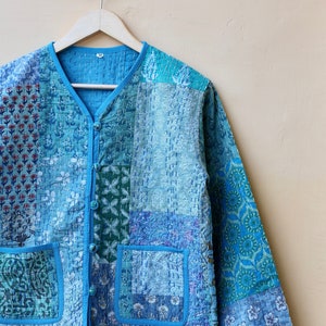 May include: A blue quilted jacket with a patchwork design. The jacket has a button closure and two pockets.