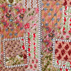 May include: A patchwork quilt with a variety of floral patterns in shades of pink, green, and brown. The quilt is quilted with a diamond pattern and has a white and black striped border.