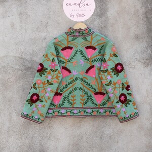 May include: A light green embroidered jacket with a floral pattern. The jacket has a high neck and long sleeves. The embroidery is in shades of pink, red, orange, and green.