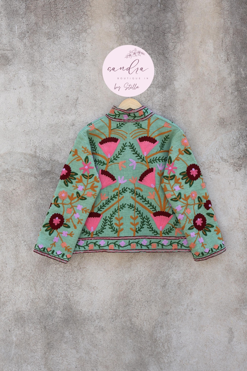 May include: A light green embroidered jacket with a floral pattern. The jacket has a high neck and long sleeves. The embroidery is in shades of pink, red, orange, and green.