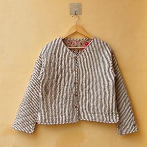 May include: A white quilted jacket with black stripes and a floral print lining. The jacket has a button closure and long sleeves.