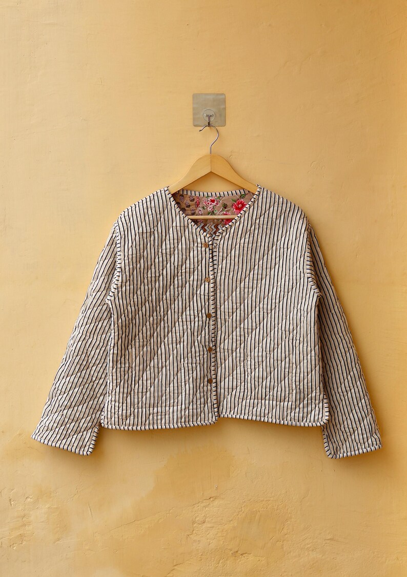 May include: A white quilted jacket with black stripes and a floral print lining. The jacket has a button closure and long sleeves.