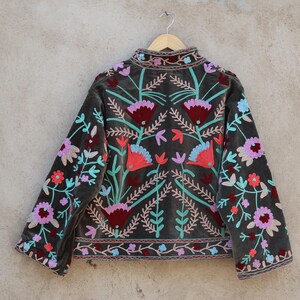 Peut inclure: Une veste en velours gris avec des broderies florales color&eacute;es. La broderie est r&eacute;alis&eacute;e avec du fil rose, rouge, bleu et vert.