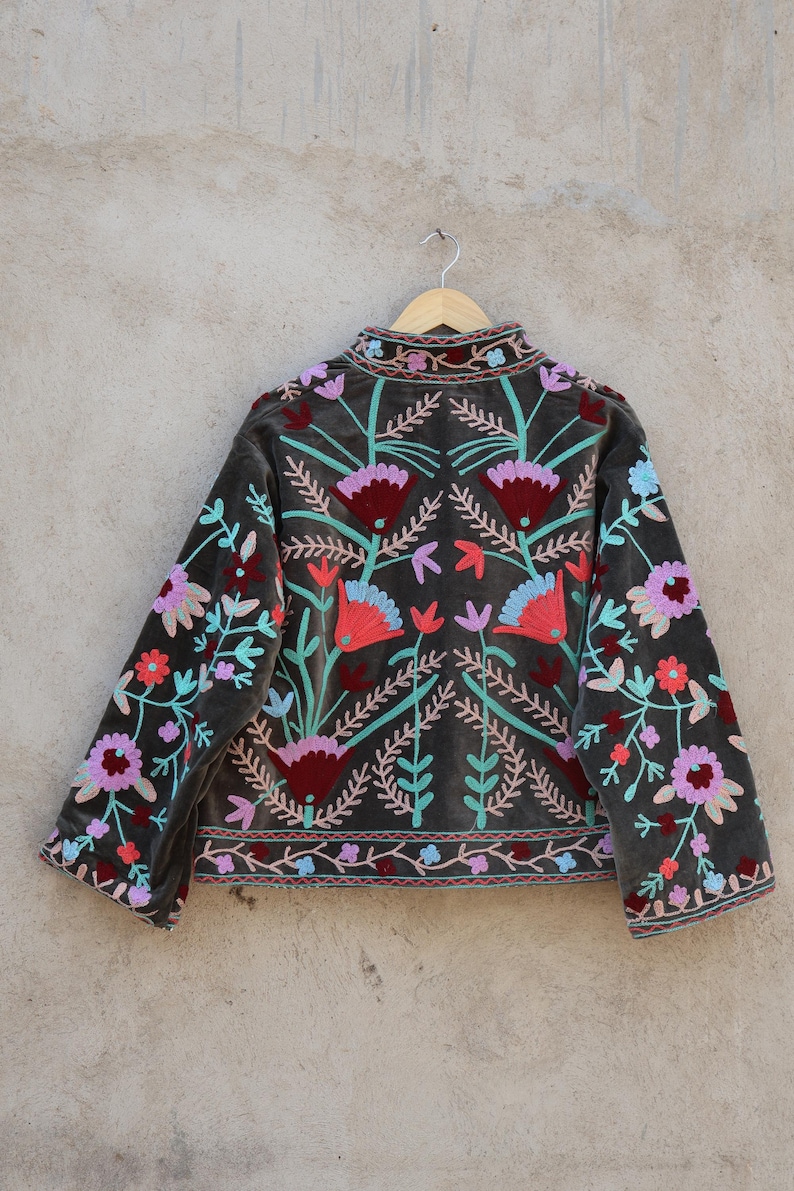 Peut inclure: Une veste en velours gris avec des broderies florales color&eacute;es. La broderie est r&eacute;alis&eacute;e avec du fil rose, rouge, bleu et vert.