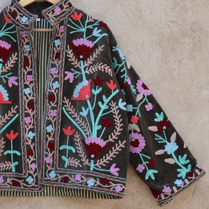 Peut inclure: Une veste en velours vert fonc&eacute; avec des broderies florales color&eacute;es. La veste a un col mandarin et des manches longues.