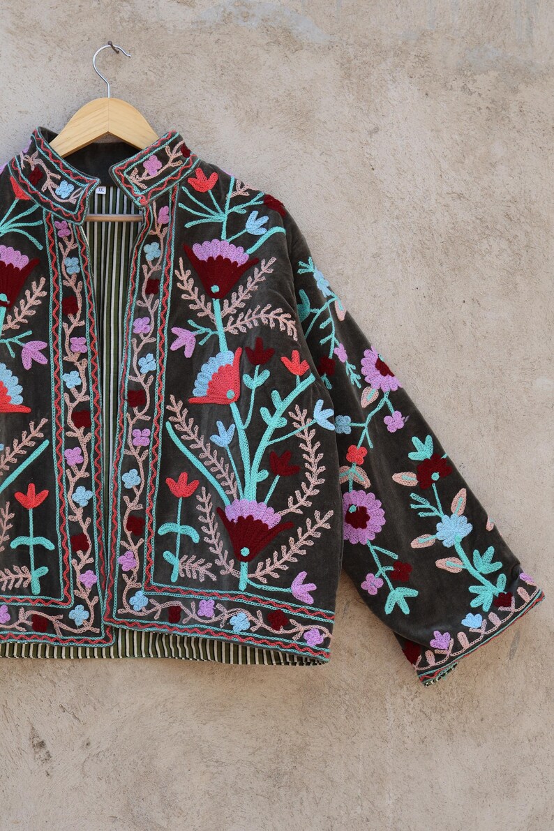 Peut inclure: Une veste en velours vert fonc&eacute; avec des broderies florales color&eacute;es. La veste a un col mandarin et des manches longues.