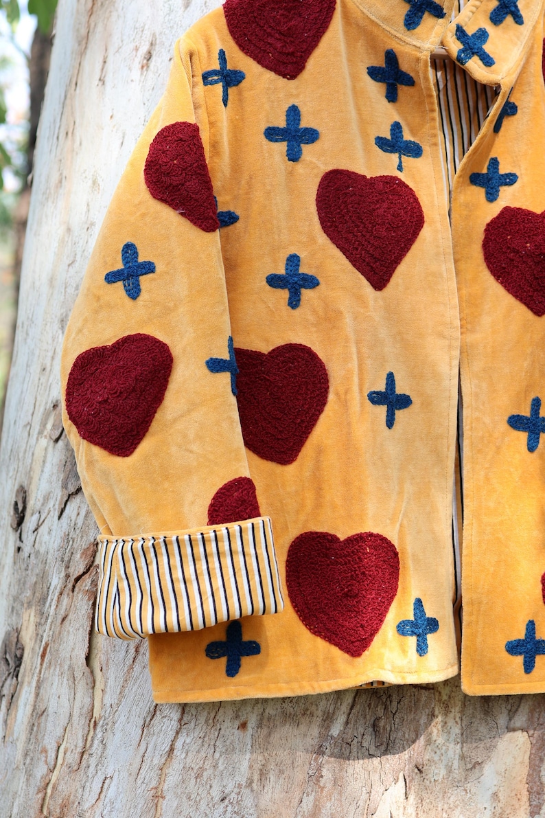 Puede incluir: Chaqueta de color amarillo mostaza con corazones rojos bordados y cruces azules. La chaqueta presenta un pu&ntilde;o a rayas y una tela suave y texturizada. Una pieza &uacute;nica, hecha a mano, para un estilo vintage o bohemio.