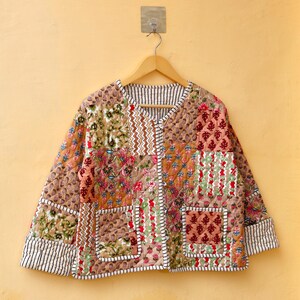May include: A brown quilted jacket with a patchwork design featuring floral and geometric patterns. The jacket has a V-neck, long sleeves, and two pockets.