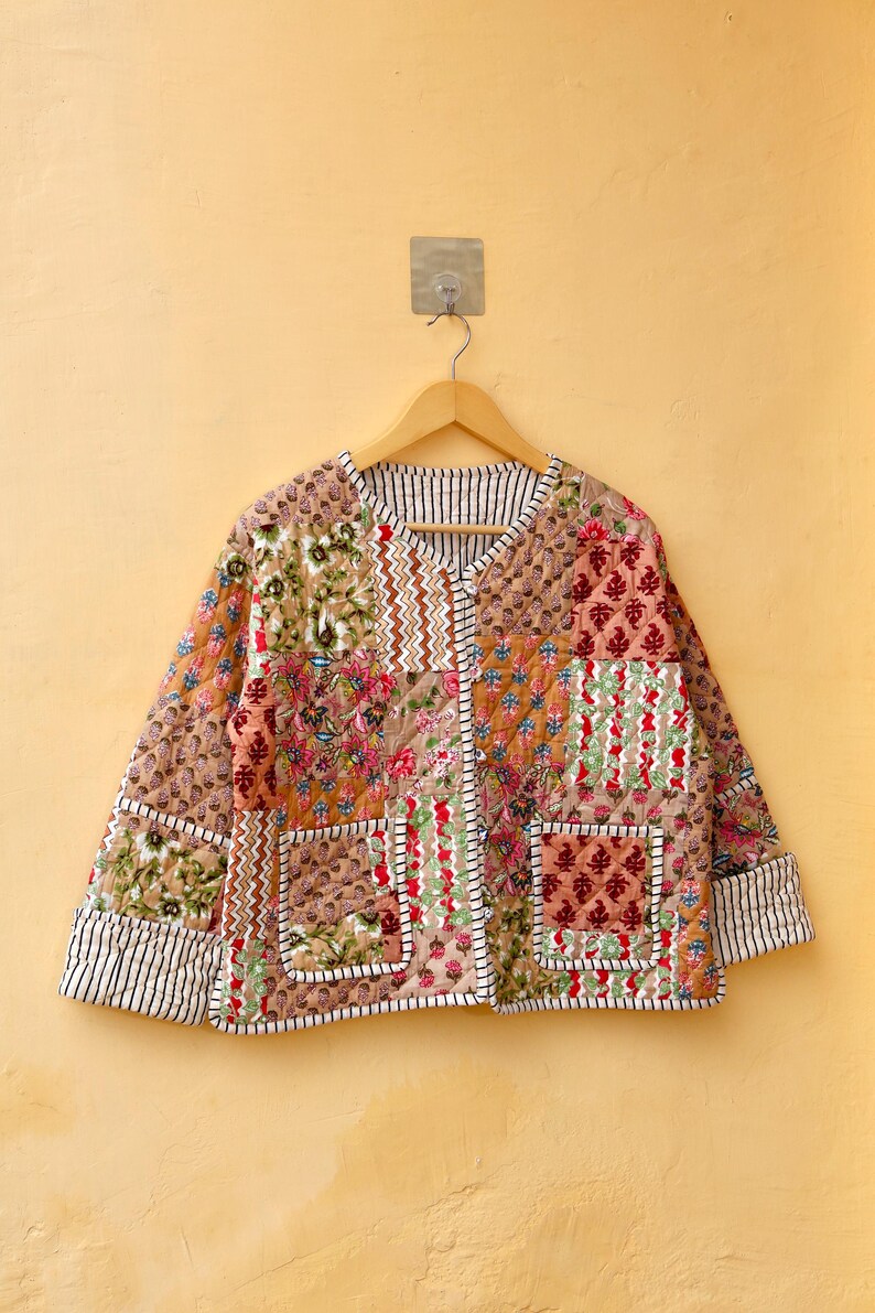May include: A brown quilted jacket with a patchwork design featuring floral and geometric patterns. The jacket has a V-neck, long sleeves, and two pockets.