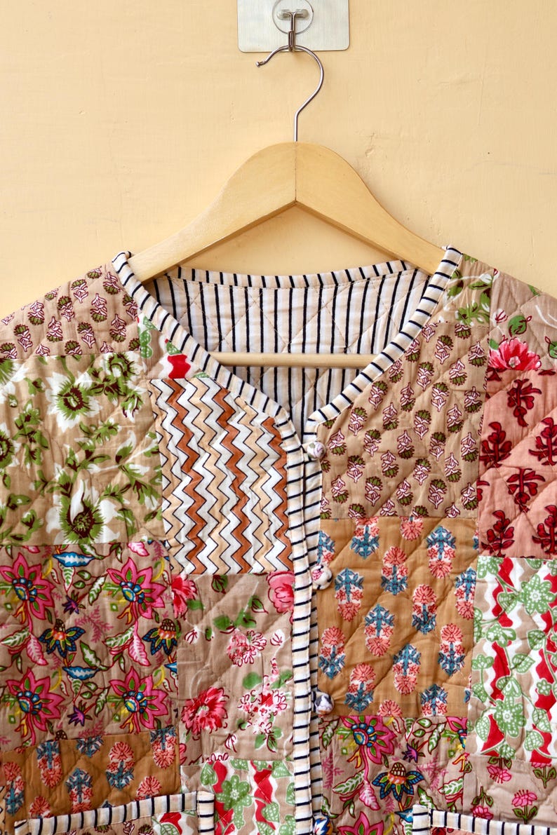 May include: A quilted jacket with a patchwork design featuring various floral patterns in shades of pink, brown, and green. The jacket has a striped trim and a button closure.