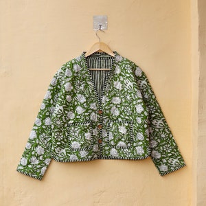 Puede incluir: Una chaqueta acolchada verde con estampado floral y ribete negro. La chaqueta tiene cierre de bot&oacute;n y dos bolsillos.