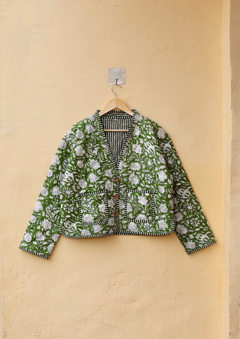 Puede incluir: Una chaqueta acolchada verde con estampado floral y ribete negro. La chaqueta tiene cierre de bot&oacute;n y dos bolsillos.