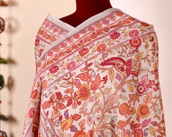May include: A white shawl with a floral and paisley pattern in shades of pink, orange, and gold. The shawl is draped over a mannequin.