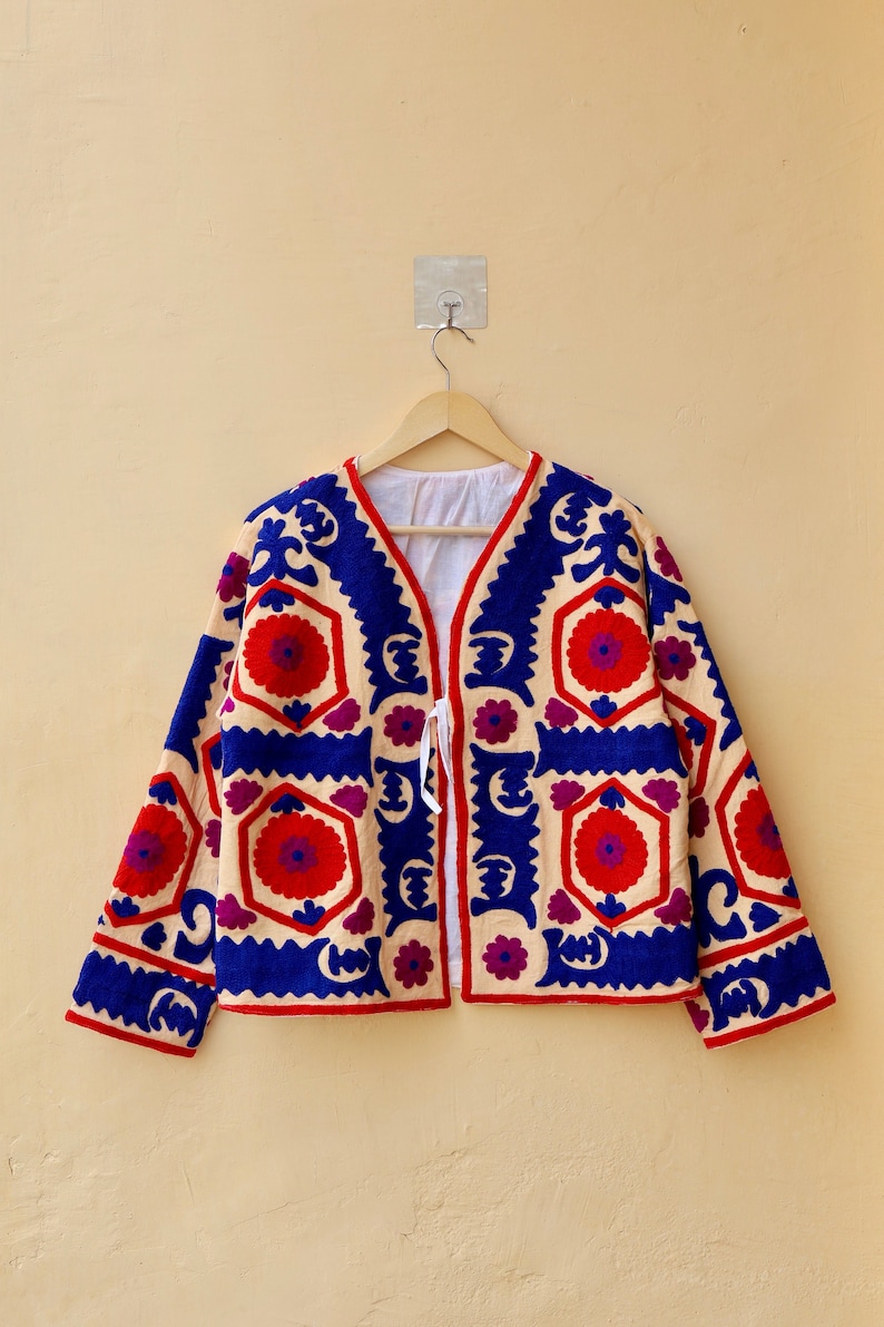 May include: A cream-colored jacket with a blue and red floral pattern. The jacket has a V-neck and long sleeves. The sleeves and hem are trimmed with red.