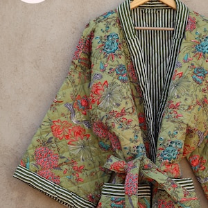 May include: A green quilted robe with a floral print and a black and white striped lining. The robe has a tie belt and is hanging on a wooden hanger.