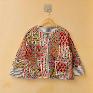 May include: A patchwork quilted jacket with a floral print in shades of brown, pink, and green. The jacket has a V-neck, long sleeves, and two patch pockets.