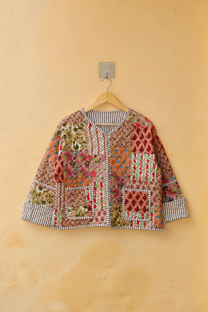 May include: A patchwork quilted jacket with a floral print in shades of brown, pink, and green. The jacket has a V-neck, long sleeves, and two patch pockets.