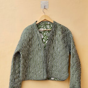 Puede incluir: Una chaqueta acolchada a rayas verdes y blancas con un forro de estampado floral. La chaqueta tiene cuello en V y mangas largas.