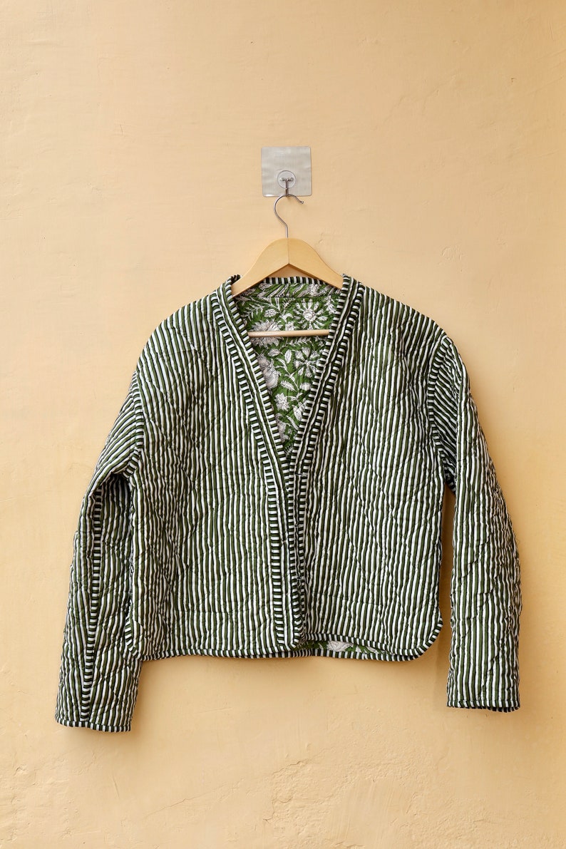 Puede incluir: Una chaqueta acolchada a rayas verdes y blancas con un forro de estampado floral. La chaqueta tiene cuello en V y mangas largas.