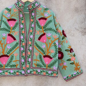 May include: A mint green embroidered jacket with floral designs in pink, orange, and burgundy. The jacket has a mandarin collar and a front closure. The text "sandra boutique 1x by Stella" is visible in the top right corner of the image.