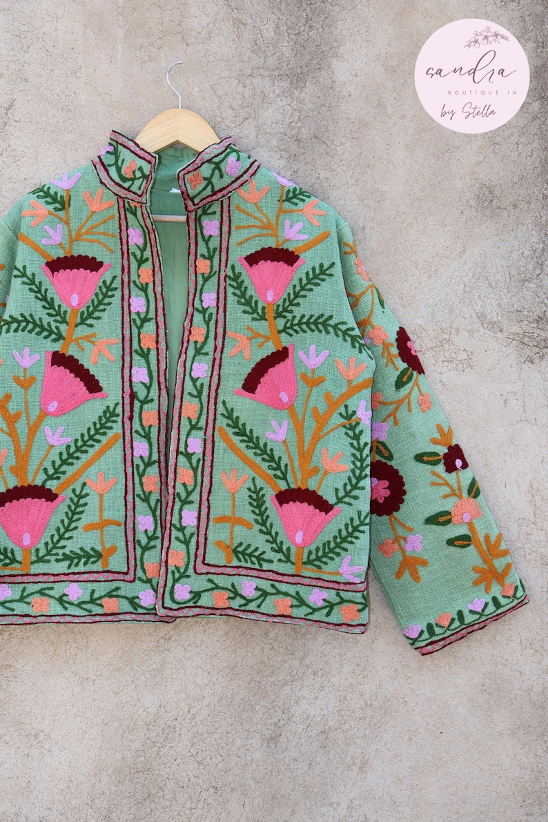 May include: A mint green embroidered jacket with floral designs in pink, orange, and burgundy. The jacket has a mandarin collar and a front closure. The text "sandra boutique 1x by Stella" is visible in the top right corner of the image.