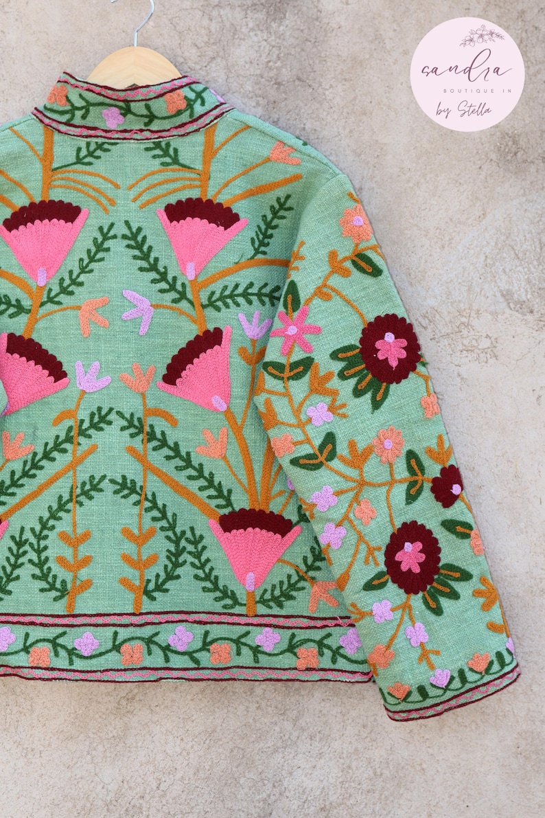 May include: A mint green jacket with floral embroidery in shades of pink, orange, and burgundy. The jacket has a mandarin collar and a button closure. The embroidery features a variety of flowers and leaves.