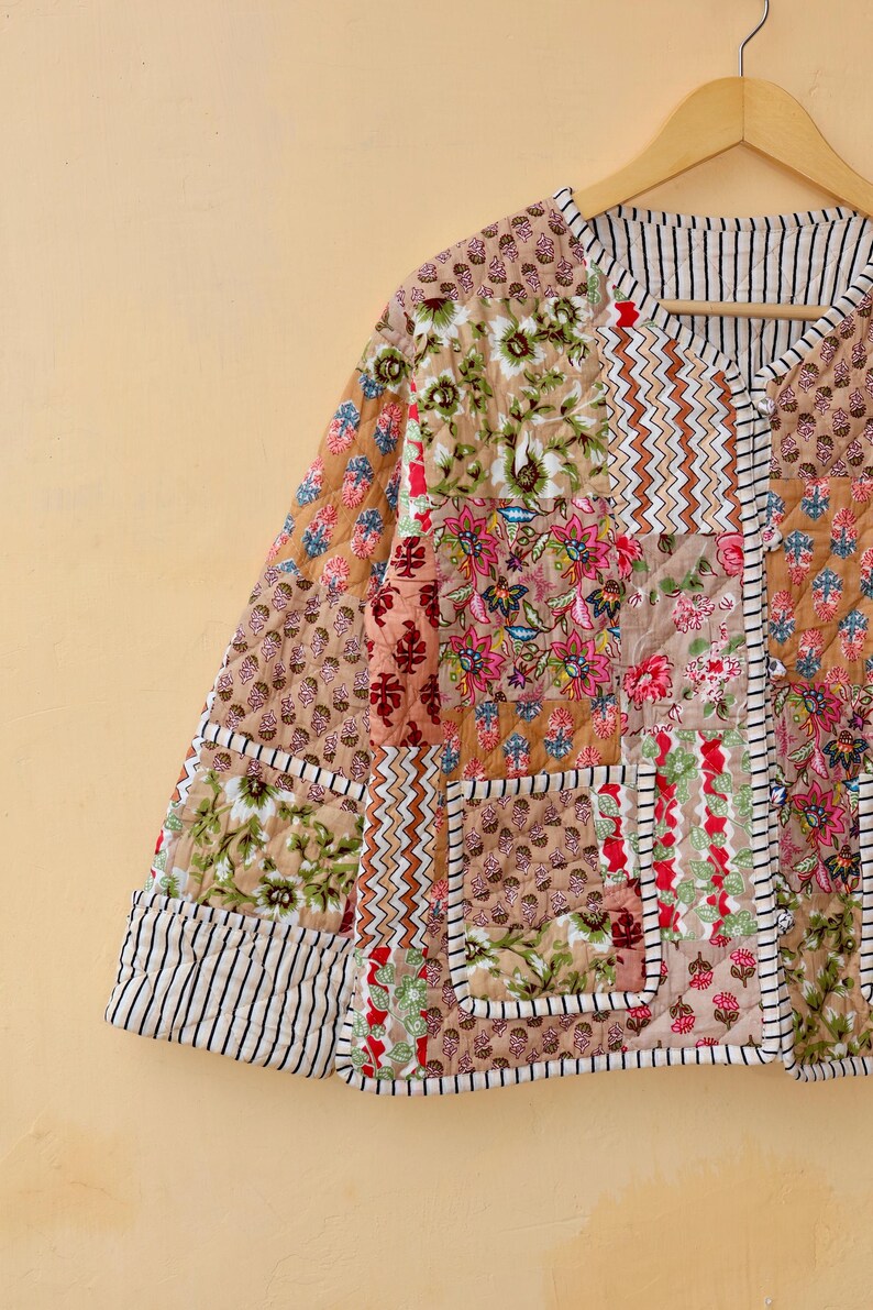 May include: A quilted jacket with a patchwork design featuring floral and geometric patterns in shades of brown, pink, and green. The jacket has a V-neck and a button closure.