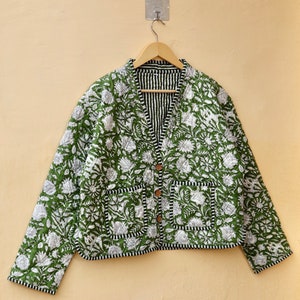 Puede incluir: Una chaqueta acolchada verde con estampado floral blanco y ribete negro. La chaqueta tiene cierre de bot&oacute;n y dos bolsillos.
