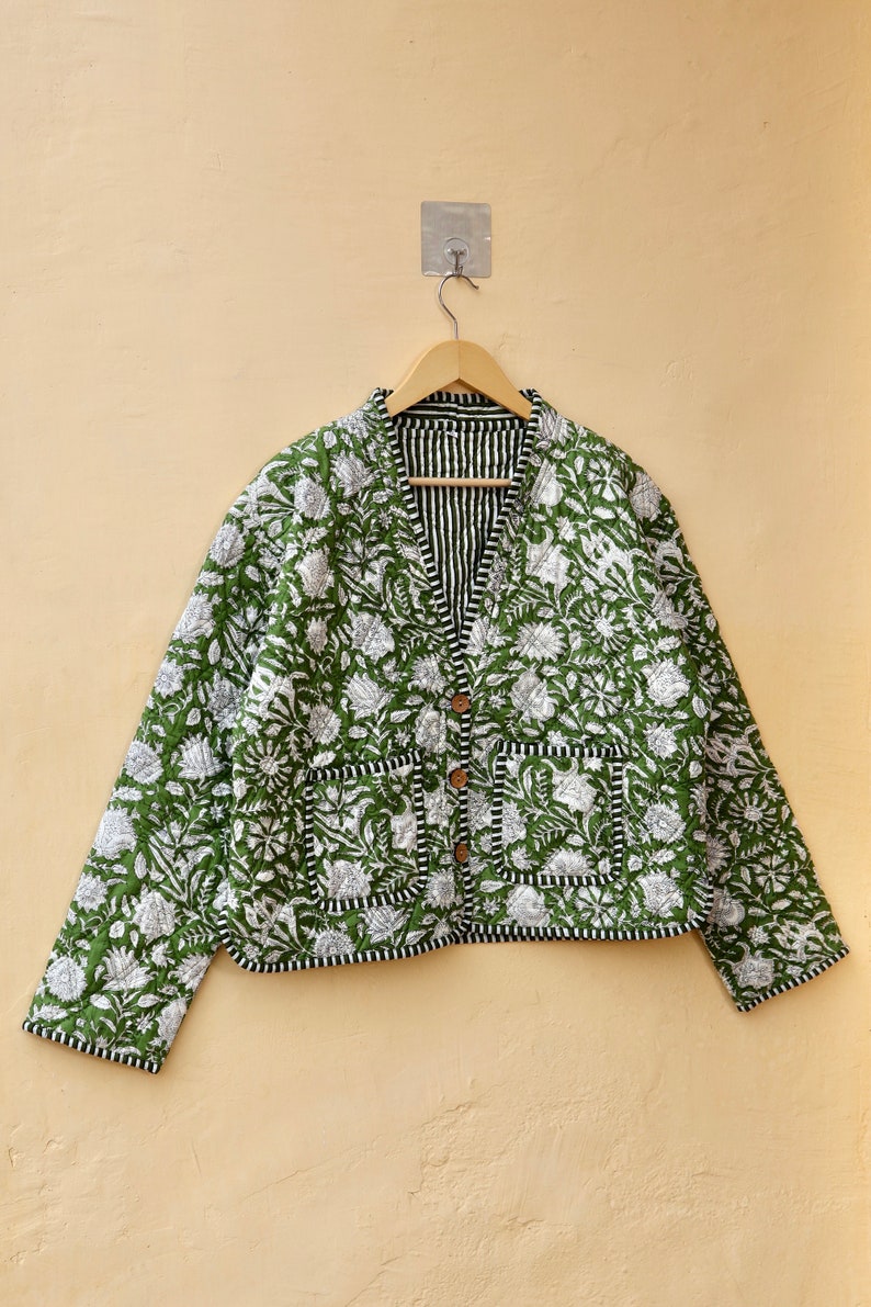 Puede incluir: Una chaqueta acolchada verde con estampado floral blanco y ribete negro. La chaqueta tiene cierre de bot&oacute;n y dos bolsillos.